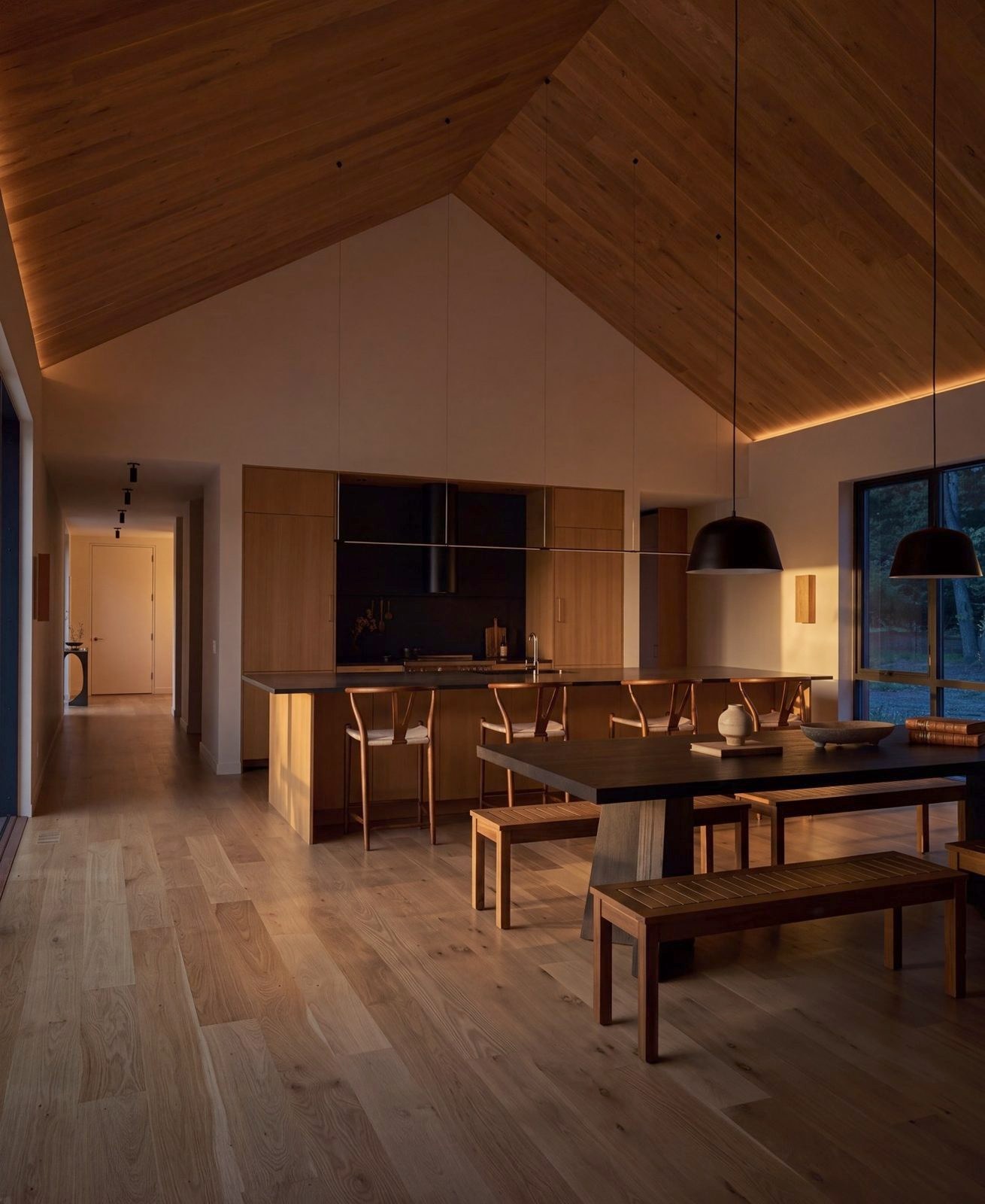 The dining table under the vaulted timber ceiling, the kitchen beyond